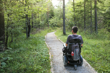 Happy man on wheelchair in nature. Exploring forest wilderness on an accessible dirt path.