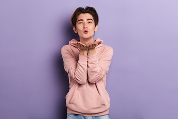 Young asian chinese man standing over isolated blue background looking at the camera blowing a kiss...