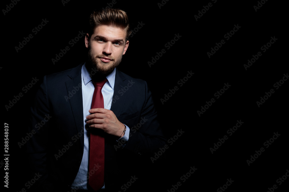 Wall mural handsome young businessman fixing tie on black background