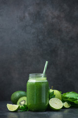 Green detox smoothie in glass jar from spinach, kiwi, lime, avocado on a dark stone table
