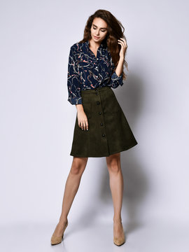 cheerful young woman posing in solitude, in a blue silk blouse with floral patterns, a dark short skirt with buttons and high-heeled shoes