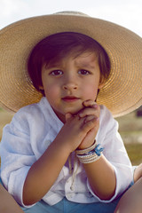 baby boy in straw hat and blue pants sitting on a haystack in a field