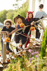 Multi-ethnic group of children wearing Halloween costumes standing on stairs of decorated house...