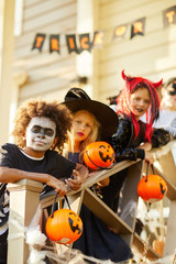 Multi-ethnic group of children wearing Halloween costumes looking at camera while standing on stairs of decorated house in trick or treat season