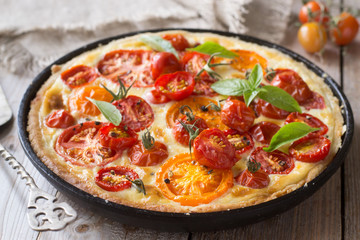 Tomato tart made with shortcrust  pastry, red and yellow tomatoes, cheese and cream. Concept of healthy eating or vegetarian food on rustic wooden background