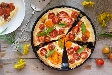 Tomato tart made with shortcrust  pastry, red and yellow tomatoes, cheese and cream. Concept of healthy eating or vegetarian food on rustic wooden background