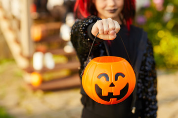 Closeup of unrecognizable little girl wearing Halloween costume and holding pumpkin basket in trick...