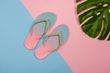 Stylish beach flip-flops on pink and blue pastel background with monstera leaf, top view. Summer minimalistic concept with copy space.