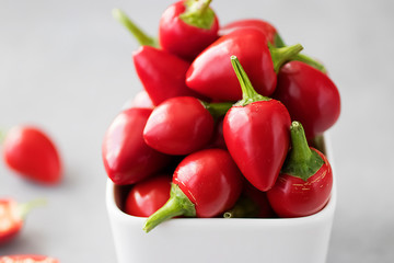 Long and round whole chili peppers in white square bowl on a gray background.