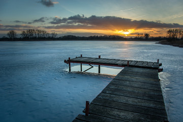 Obraz premium Jetty on a frozen lake, clouds and sunset