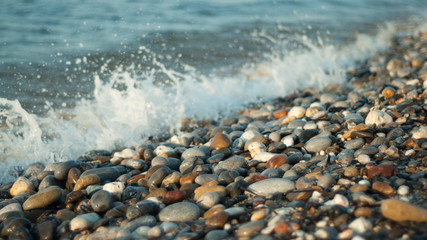 Mediterranean sea coast with pebbles at sunset. Close up wave with white foam in Greece.
