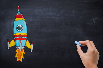 Chalkboard or blackboard with hand drawn cartoon rocket and hand ready to add copy or text