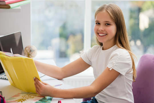 Smiling school preteen girl reading book at table