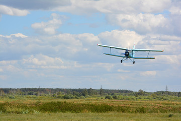 The airplane AN-2 is coming down over green grass for landing
