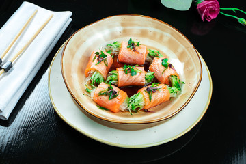 Close up on creative made sushi roll with salmon, microgreen, cucumber. Delicious salmon sashimi in yellow bowl with soy sauce on dark background. Japanese cuisine. Seafood, raw fish.