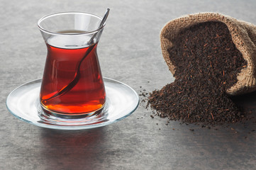 Glass Turkish brewed black tea with dry black tea in burlap sack on black rustic background. Turkish traditional hot drink 