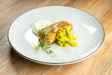 Salmon steak with mango and white sauce on a white plate on a wooden background. Restaurant serving dishes. Delicious seafood dish. Fish. Food photo for menu or recipe