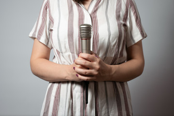 A wireless microphone in a woman hands on a gray background.