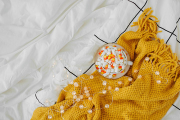 Coffee with marshmallow and candy corn on bed with warm plaid. Autumn beverage, Breakfast in bed. Hygge concept.