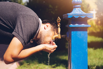 Caucasian young man preparing to drinking water from the retro fountain.