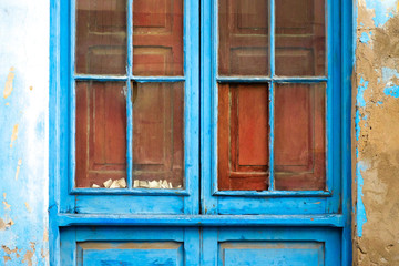 Blue weathered window frame with broken glass and aged wall sections, old derelct and abandoned house detail in Latino district