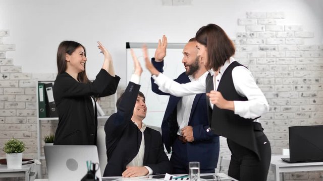 Team of happy business people looking at screen of laptop making winner gesture celebrating victory