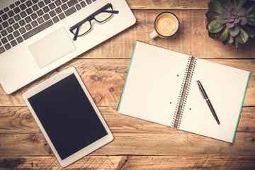Laptop, computer tablet and open note book with white copy space on a rustic wooden table. Office...