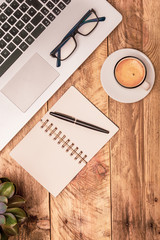Vertical top view composition of modern office workspace with laptop, note book, coffee and plant...