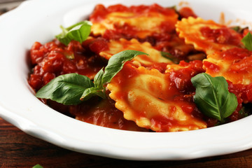 Ravioli with tomato sauce garnished with parmesan cheese and basil on rustic table