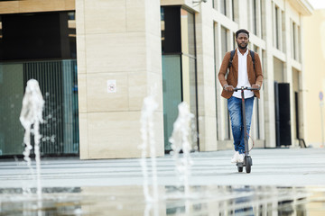 Front view portrait of contemporary African-American man riding electric scooter in urban setting...