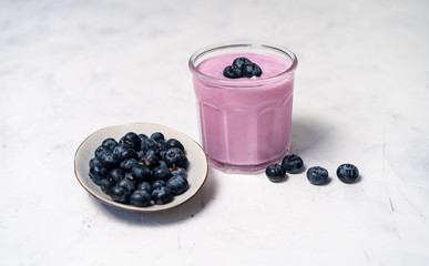 Tasty fresh blueberry yoghurt shake dessert in glass standing on white table background.