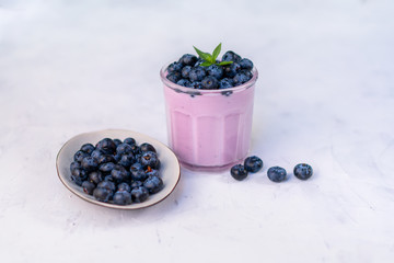 Tasty fresh blueberry yoghurt shake dessert in glass standing on white table background.