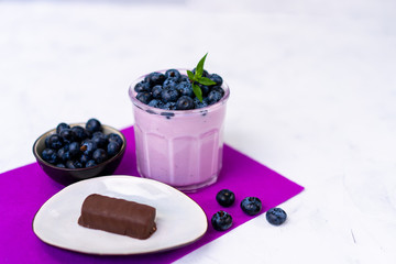 Tasty fresh blueberry yoghurt shake dessert in glass standing on white table purple napkin background.