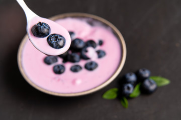 Tasty fresh blueberry yoghurt shake dessert in ceramic bowl standing on black dark table background.