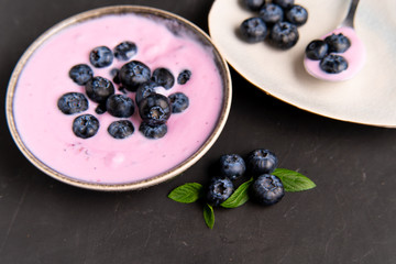 Tasty fresh blueberry yoghurt shake dessert in ceramic bowl standing on black dark table background.