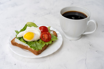 Sandwich with fried eggs salad and tomato on a white plate on a white background.