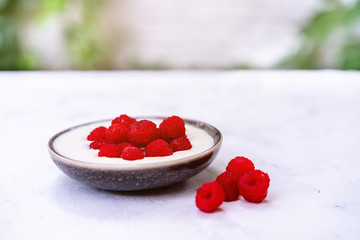 Tasty fresh raspberries yoghurt shake dessert in ceramic bowl standing on white table background.