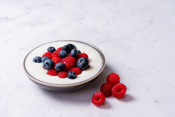 Tasty fresh blueberry raspberries yoghurt shake dessert in ceramic bowl standing on white table background.