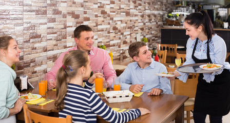 Obraz na płótnie Canvas smiling brunette waitress serving family in family cafe