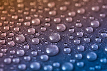 Water drops on shiny and grainy metal surface, abstract blue and yellow background with wet drops