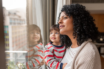 Mother and cute daughter looking through a window at home