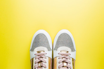 Fashion blog look. White women's sneakers with pink and gold color on yellow background. Flat lay, top view beauty female background.