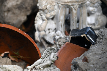 A white, damaged small sculpture of a sleeping angel in front of two another damaged angels. 