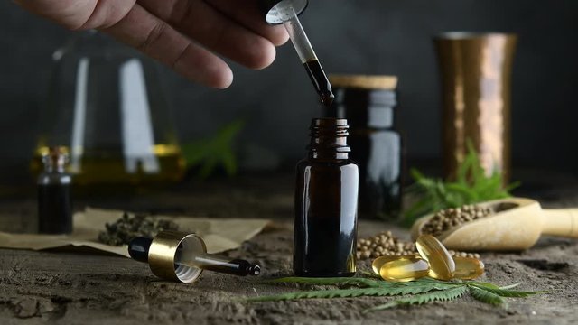 hemp essential oil in small glass bottle. container with cannabis leaves and cannabis seeds on wooden.