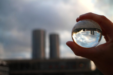glass crystal ball in hand and  a reflection in the style of a factory town,  symbolizing the fragility of nature and the world - Powered by Adobe