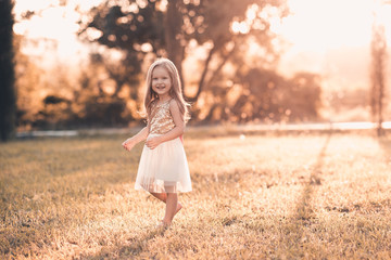 Happy child girl 4-5 year old wearing stylish princess dress walking in park over sunset light....