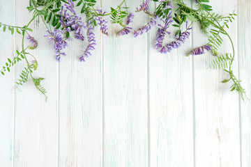Fototapeta na wymiar Light wooden background with lilac wild curly flowers. Floral natural background. Summer flowers