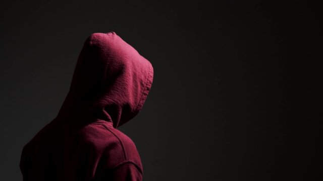 Young male wearing red hoodie vaping in a dark alley