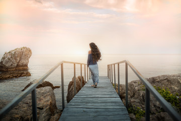 Woman walks on the bridge against the background of the sunset sea.