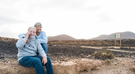 Senior man with white beard calls with cellphone. Couple with gray hair, casual clothing. Hug and tenderness. Early morning waiting the sun